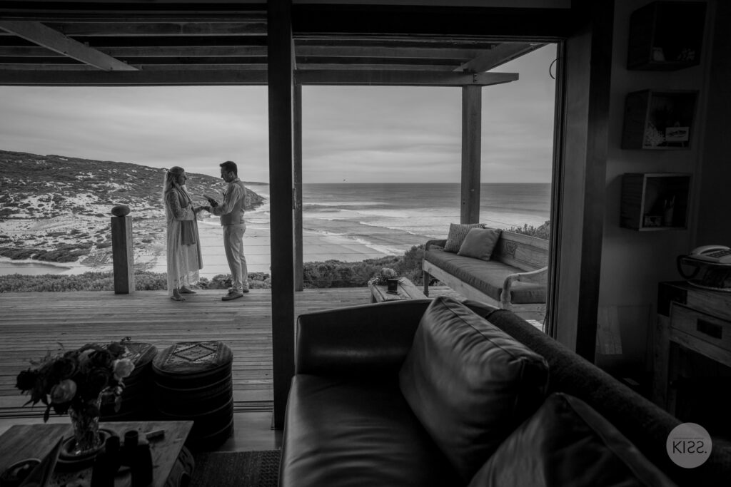 A couple seen through the dark frame of a coastal cottage doorway, in black and white
