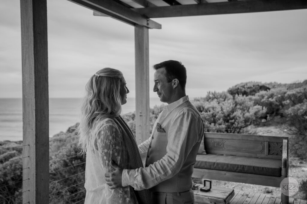 A couple during their ceremony with the sea beyond, in black and white
