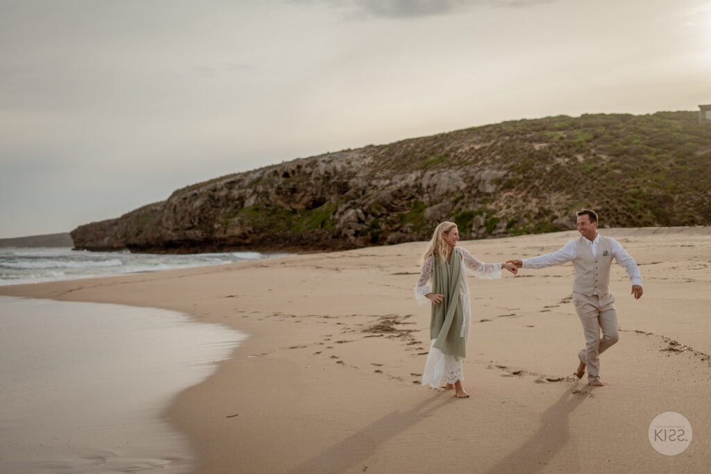 A couple walking hand in hand along a wide beach beneath a clouded sky