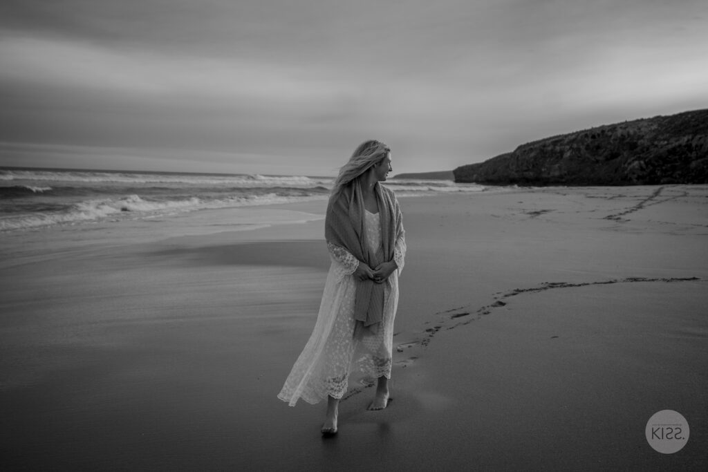 A lone figure on the beach beneath an open sky, in black and white